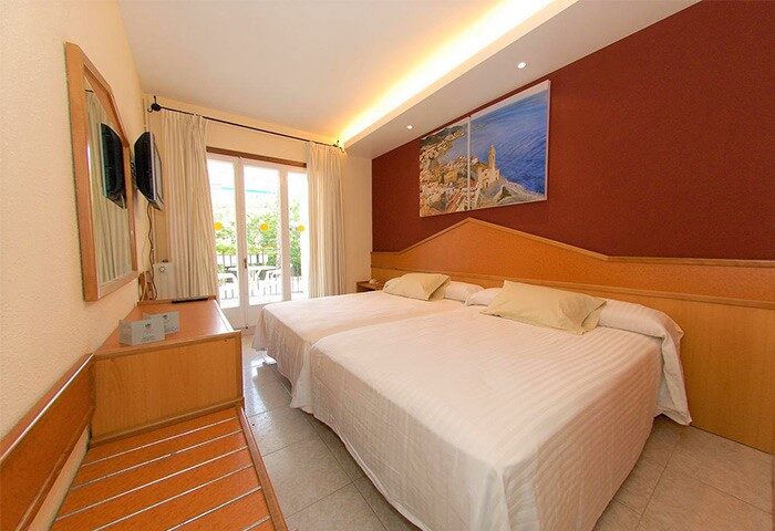 Galeon, gay-friendly hotel room. Twin beds with white linens, wood headboard, balcony, and artwork. Ideal for gay men's travel.