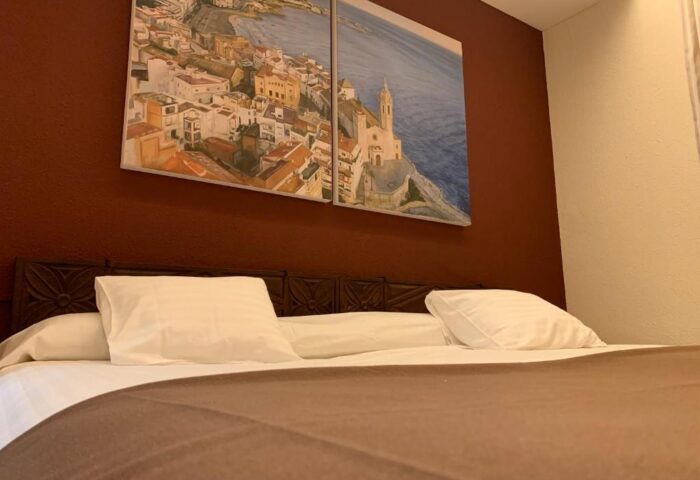 Galeon Gay-Friendly Hotel room with bed, pillows, and a painting of a coastal town on the wall. A great choice for gay men travelers.