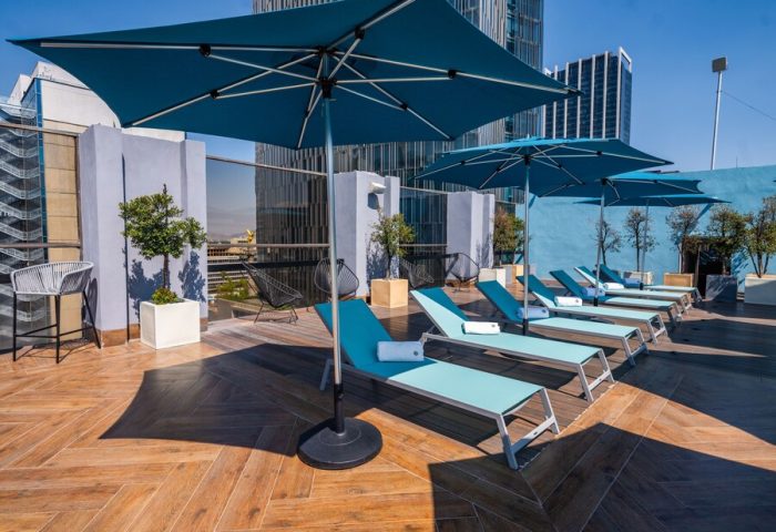 Galeria Plaza Reforma gay-friendly hotel rooftop pool. Blue umbrellas shade lounge chairs on wood deck. Modern Mexico City hotel for gay travelers.