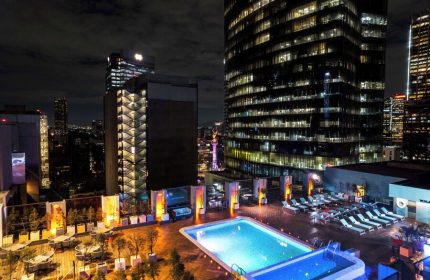 Night view of Galeria Plaza Reforma, a gay-friendly hotel. Pool, lounge chairs, and city lights create a relaxing rooftop scene. Mexico City travel.