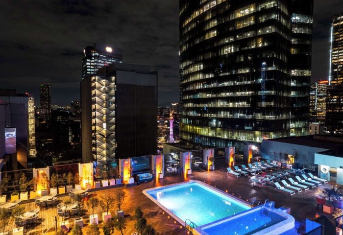 Night view of Galeria Plaza Reforma, a gay-friendly hotel. Pool, lounge chairs, and city lights create a relaxing rooftop scene. Mexico City travel.
