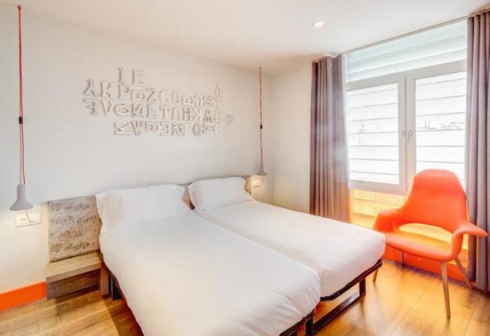 Generator Barcelona hotel room. Pet-friendly, gay-friendly hotel with twin beds, modern design, and bright orange chair. Great for gay travel.