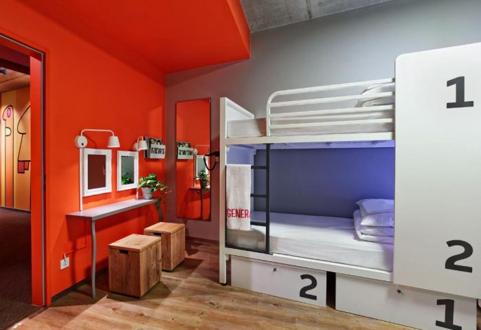 Generator Berlin Mitte gay-friendly hotel room. Bunk beds with lockers, orange wall, mirrors, and wooden stools. Modern hostel design.