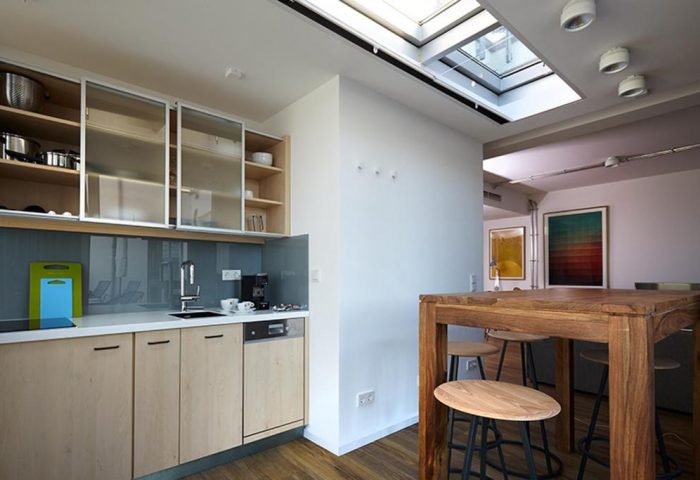 Kitchen area in Generator Berlin Mitte, a gay-friendly hotel. Modern design with skylight, wooden table, and stools. Ideal for gay travel.