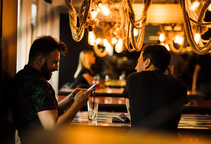 Generator Copenhagen gay-friendly hotel: Two men at the bar, one looking at his phone, under a rope light fixture.