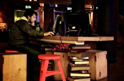 Generator Hostel Dublin review: Man using computer at a desk made of books. Gay-friendly hotel with unique design elements.