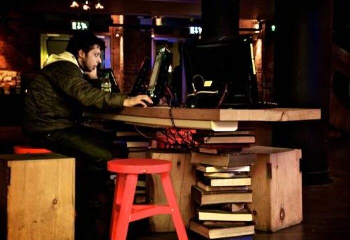 Generator Hostel Dublin review: Man using computer at a desk made of books. Gay-friendly hotel with unique design elements.