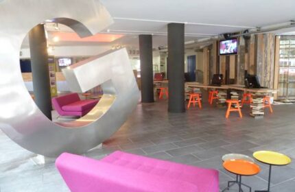 Generator Hostel Dublin lobby with pink sofas, colorful tables, and a large G sculpture. Gay-friendly hotel with modern design. Reviews available.