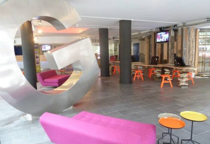 Generator Hostel Dublin lobby with pink sofas, colorful tables, and a large G sculpture. Gay-friendly hotel with modern design. Reviews available.