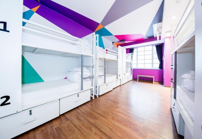 Generator London gay-friendly hotel pet-friendly room. Bunk beds line a hostel room with colorful geometric ceiling art. Wood floor, white linens.