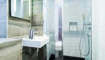 Bathroom at Gay-Friendly Generator London Hotel. Shower with glass door, black tile floor, sink, and mirror. Pet-friendly hotel for gay men travel.