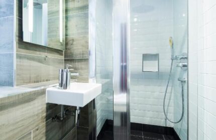 Bathroom at Gay-Friendly Generator London Hotel. Shower with glass door, black tile floor, sink, and mirror. Pet-friendly hotel for gay men travel.