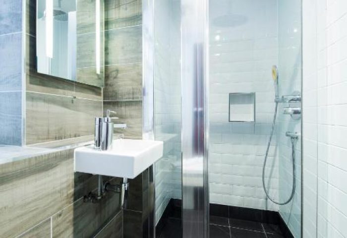 Bathroom at Gay-Friendly Generator London Hotel. Shower with glass door, black tile floor, sink, and mirror. Pet-friendly hotel for gay men travel.