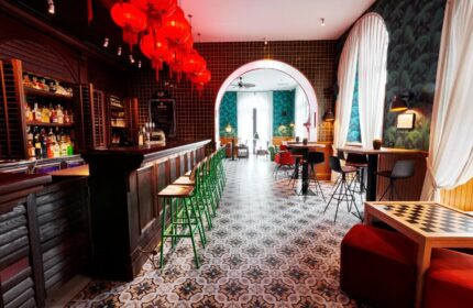 Generator Rome, a gay-friendly hotel. Bar with red lanterns, green stools, patterned floor, and tropical wallpaper. A stylish, inclusive space.