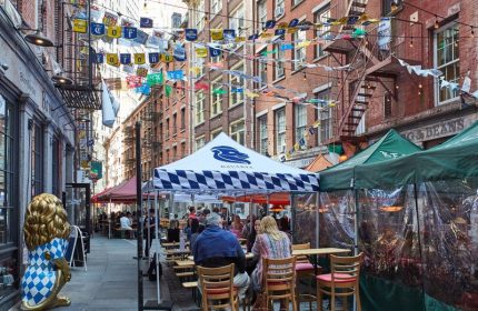 Outdoor dining at Gild Hall, A Thompson Hotel By Hyatt. A gay-friendly hotel in NYC, with tents, flags, and a lion statue.