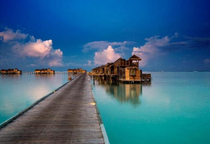 Gili Lankanfushi Maldives gay-friendly hotel. Overwater bungalows on a wooden pier, turquoise water, and blue sky. Perfect for gay travel.
