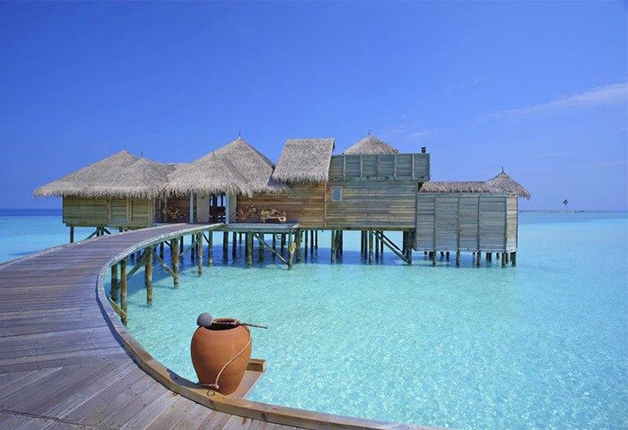 Gili Lankanfushi Maldives gay-friendly hotel. Overwater bungalow with a thatched roof, wooden walkway, and turquoise water. Gay travel luxury.