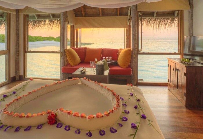 Romantic suite at Gili Lankanfushi, Maldives. Heart-shaped towels & flowers on bed. Gay-friendly hotel with ocean views. Luxury travel.