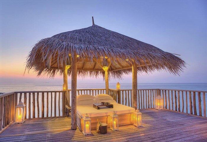 Gili Lankanfushi Maldives gay-friendly hotel. Thatched roof gazebo with bed, lanterns, and ocean view. Romantic getaway for gay men travelers.