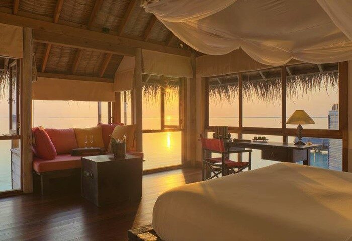 Gili Lankanfushi Maldives gay-friendly hotel room with sunset view. Luxurious interior, cozy seating, and desk setup. Perfect for gay travel.