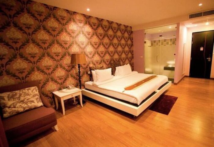 Glitz Hotel room interior. Gay-friendly hotel with a double bed, patterned wallpaper, armchair, and glass-enclosed shower. Stylish gay travel lodging.