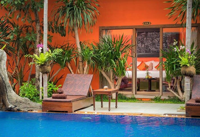 Poolside view of Gay-Friendly Golden Temple Hotel room. Chaise lounge, tropical plants, and orange wall. Gay travel advice for Siem Reap.