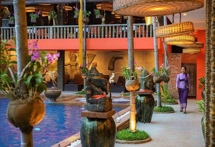 Gay-friendly Golden Temple Hotel pool area. Woman in purple uniform. Wicker lamps, statues, and plants. Siem Reap gay travel.
