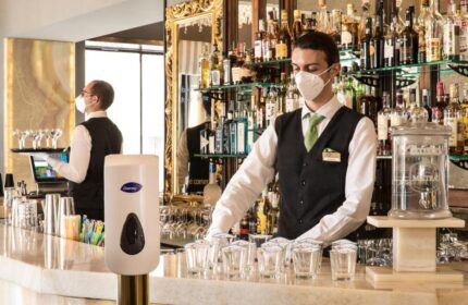 Bar at the Gay-Friendly Golden Tulip Rome Piram hotel. Bartender in mask prepares drinks. Safe & stylish travel for gay men in Rome.