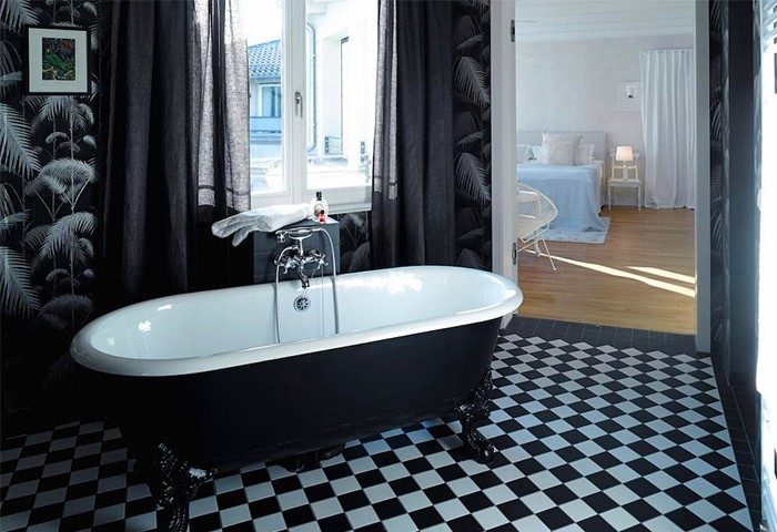 Gorki Apartments' bathroom with a clawfoot tub, black and white checkered floor, palm wallpaper, and a view into the bedroom. Pet-friendly hotel.