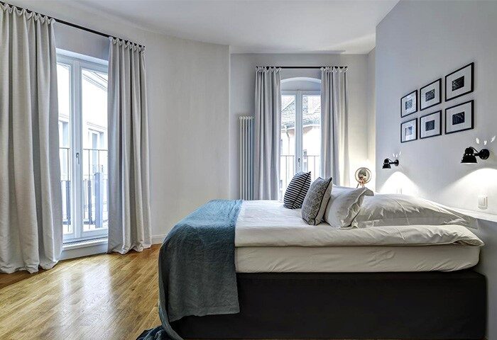 Gorki Apartments bedroom: Gay-friendly, pet-friendly hotel. Modern design, light walls, wood floor, bed with blue throw, & balcony access.