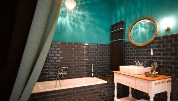 Gorki Apartments gay-friendly hotel bathroom. Dark tile, turquoise walls, vintage-style vanity, bathtub, and chandelier. Pet-friendly space.