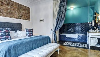 Gorki Apartments pet-friendly suite. Bedroom with a blue bedspread, bench, and bathroom with blue tiles. Gay-friendly hotel for gay travelers.