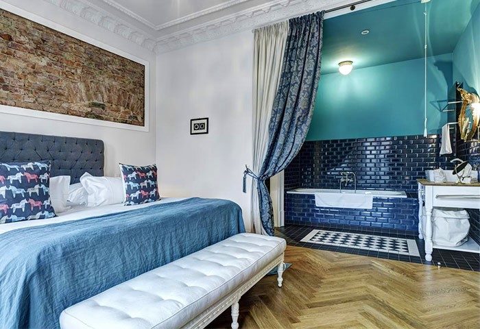 Gorki Apartments pet-friendly suite. Bedroom with a blue bedspread, bench, and bathroom with blue tiles. Gay-friendly hotel for gay travelers.