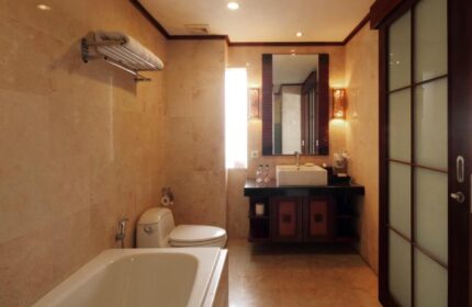 Bathroom at Grand Balisani Suites Hotel, a gay-friendly hotel. Features a bathtub, toilet, sink, mirror, and marble walls. Bali travel.