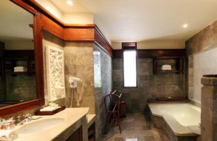 Bathroom at Grand Balisani Suites Hotel, a gay-friendly hotel. Features a bathtub, sink, mirror, and stone tile. Ideal for gay men's travel.