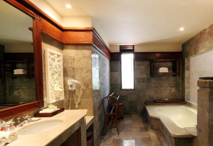 Bathroom at Grand Balisani Suites Hotel, a gay-friendly hotel. Features a bathtub, sink, mirror, and stone tile. Ideal for gay men's travel.
