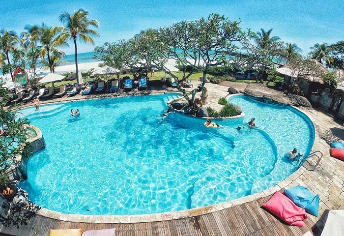 Grand Balisani Suites Hotel pool view. Gay-friendly hotel with palm trees, beach, and clear blue water. Perfect for gay travel advice.