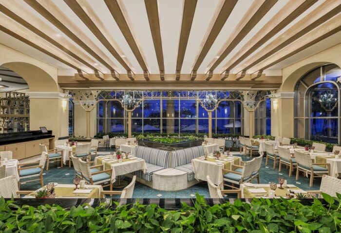 Dining area at Grand Fiesta Americana Coral Beach Cancun All Inclusive, a gay-friendly hotel. Tables with white cloths, wicker chairs, and greenery.