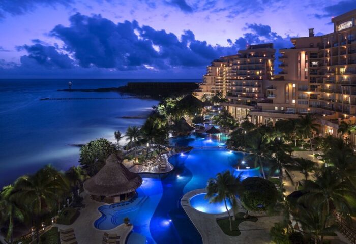 Grand Fiesta Americana Coral Beach Cancun All Inclusive at night. Gay-friendly hotel with pools, palm trees, ocean view. Luxury travel.