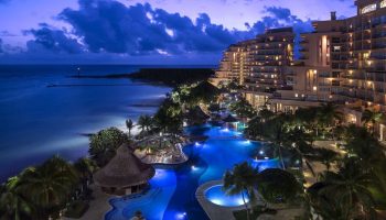 Grand Fiesta Americana Coral Beach Cancun All Inclusive at night. Gay-friendly hotel with pools, palm trees, ocean view. Luxury travel.