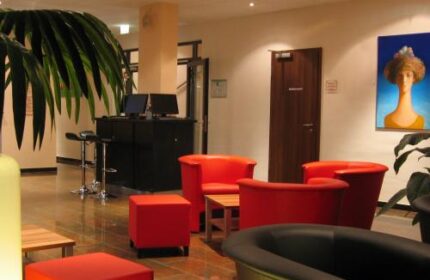 Grand Hotel Dream Main City Center lobby. Gay-friendly hotel interior with red chairs, bar stools, and modern art. A welcoming space.