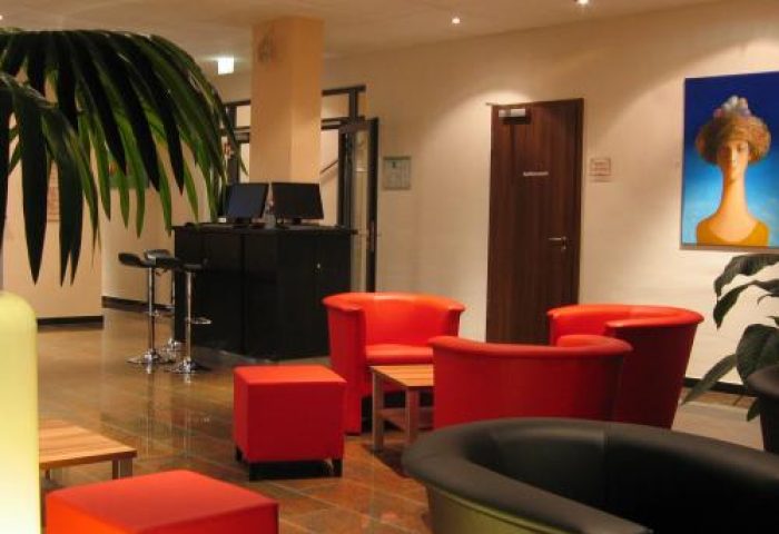 Grand Hotel Dream Main City Center lobby. Gay-friendly hotel interior with red chairs, bar stools, and modern art. A welcoming space.