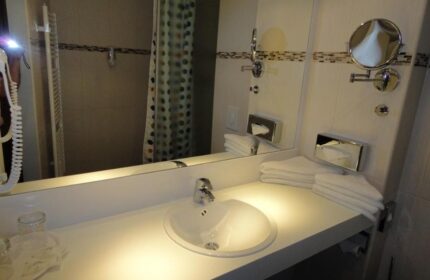 Bathroom at Grand Hotel Dream Main City Center, a gay-friendly hotel. Sink, mirror, and shower curtain visible.
