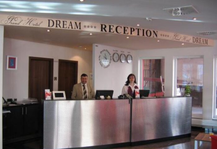 Grand Hotel Dream Main City Center reception desk with staff. Gay-friendly hotel. Clocks showing different time zones.