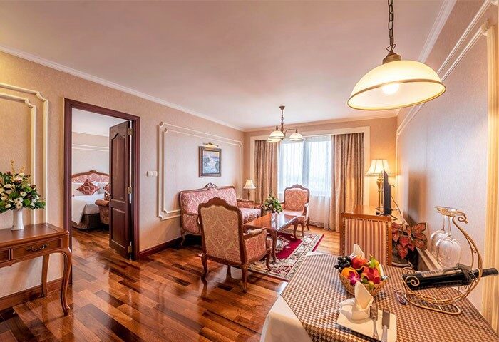 Grand Hotel Saigon suite. Gay-friendly hotel room with living area, dining table, and bedroom view. Elegant, comfortable space for LGBT travelers.
