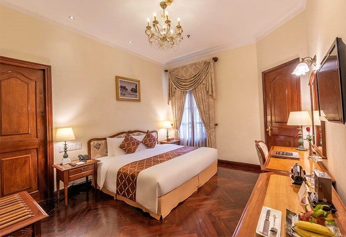 Grand Hotel Saigon gay-friendly room. Elegant decor, chandelier, wood floors, desk, and a large bed. Perfect for gay travelers.