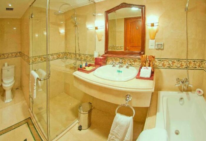 Grand Hotel Saigon bathroom. This gay-friendly hotel features a shower, sink, mirror, and bathtub in a luxurious setting.