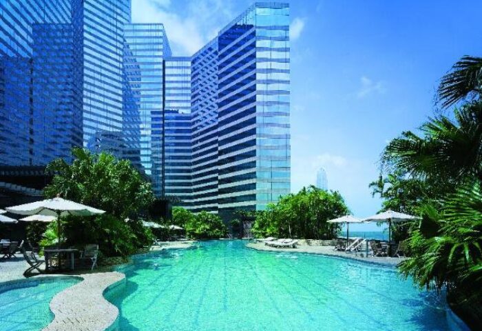 Grand Hyatt Hong Kong's pool. Gay-friendly hotel with turquoise pool, umbrellas, palm trees, and modern buildings. Ideal for gay travel.