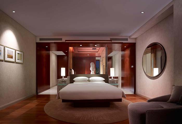 Grand Hyatt Kuala Lumpur Hotel room. Modern design with a bed, round mirror, and wooden accents. Gay-friendly hotel for gay travelers.
