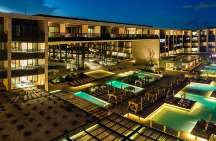 Grand Hyatt Playa Del Carmen Resort at night. Gay-friendly hotel with pools, lounge chairs, and modern architecture. Luxury travel destination.